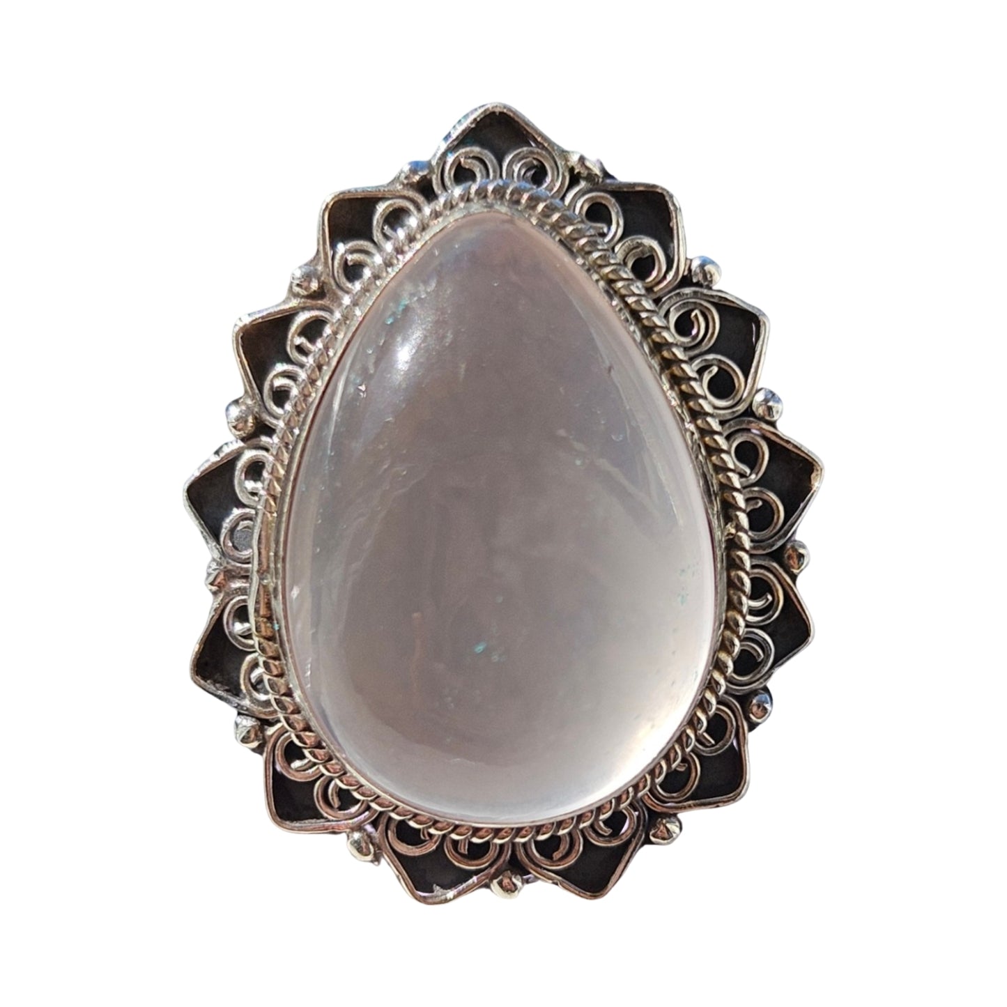 A teardrop-shaped silver ring featuring a smooth, pale Rose quartz cabochon gemstone in the center, surrounded by an ornate filigree silver border with dark inlay details